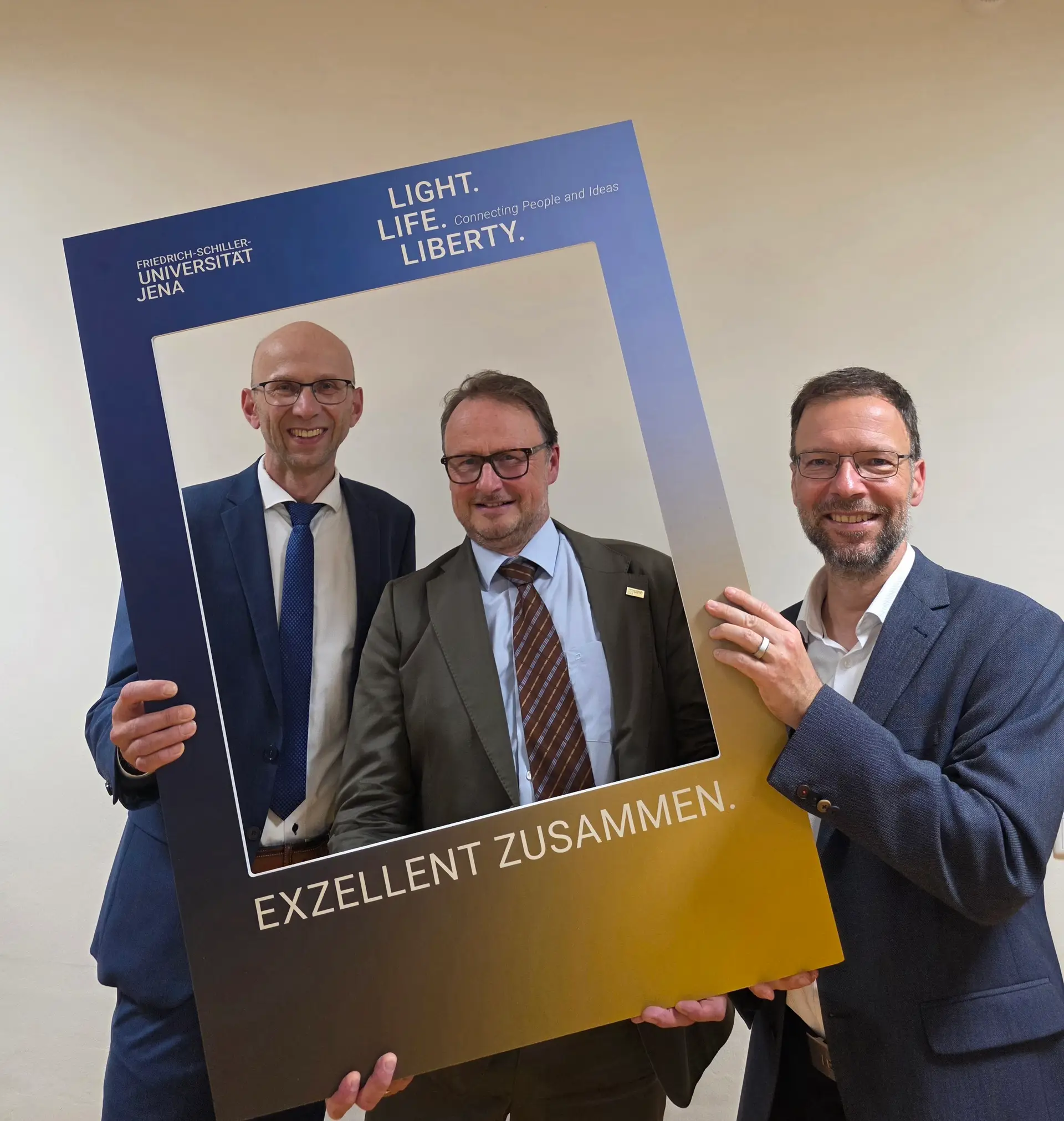 Zwei Männer gratulieren einer dritten Person: Wilfried Röpke (links) und Oberbürgermeister Dr. Thomas Nitzsche (rechts) stehen mit Prof. Andreas Marx, dem Präsidenten der Friedrich-Schiller-Universität Jena, zusammen.
